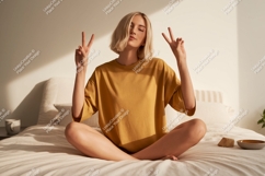 Young woman peace gesture on bed blonde yellow Product Image 1