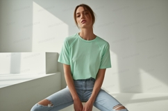 Woman wearing mint green t shirt and ripped jeans image Product Image 1