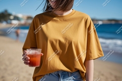 Woman wearing mustard t shirt holding drink on beach Product Image 1