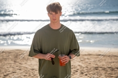 Young man holding drink sunglasses beach ocean sand Product Image 1