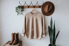 Beige sweatshirt hanging on rack with hat boots and plant Product Image 1