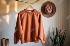 Orange sweatshirt hanging on branch with hat and plant Product Image 1
