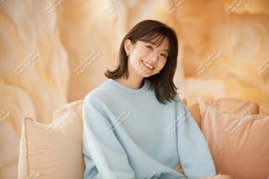 Young woman smiling wearing blue sweatshirt on couch Product Image 1