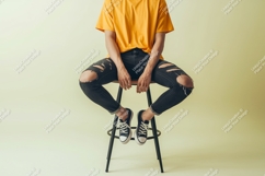Person wearing yellow t shirt ripped jeans sitting on stool Product Image 1