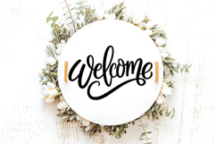 Minimal black welcome lettering with a stylish script font and extended tail flourish, perfect for entryway signs or door hangers. Displayed on a soft neutral wood background for scale and clarity.