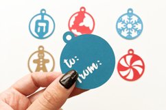 6 round winter holiday themed gift tag SVG designs. One is held by a hand.
