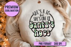 Blond girl standing in front of Christmas tree holding a present wearing a white sweatshirt with Santa's hoes design on it