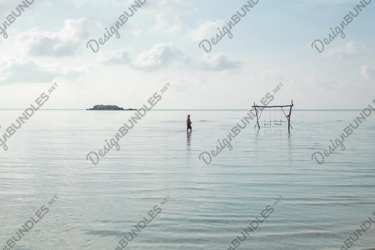 Lonely woman and wooden swing in the middle of sea shallow