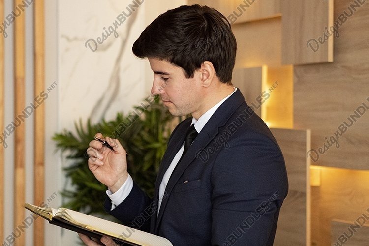 businessman in a dark blue suit writing in diary in office