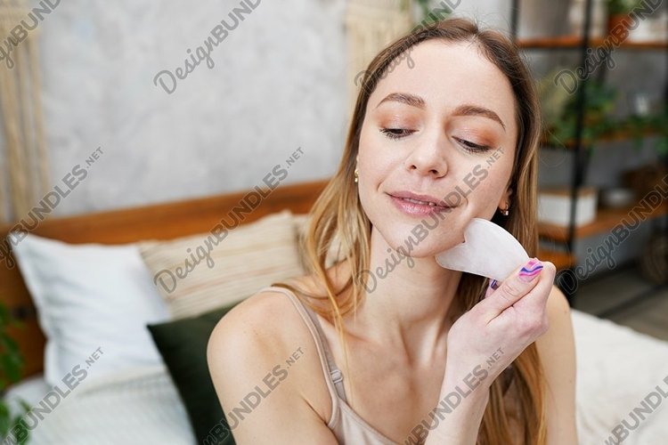 Young woman is doing Gua Sha facial massage in bathroom