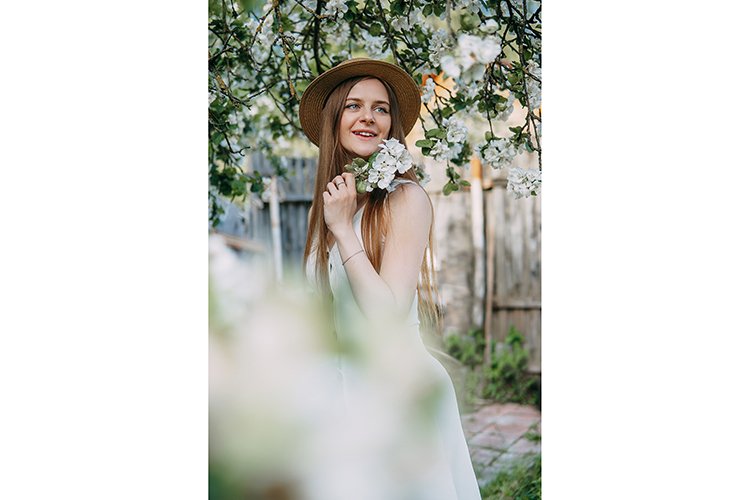 Beautiful young girl in hat in blooming Apple orchard.