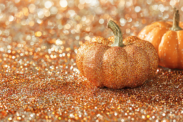 Glittery orange pumpkin sits on sparkling orange background
