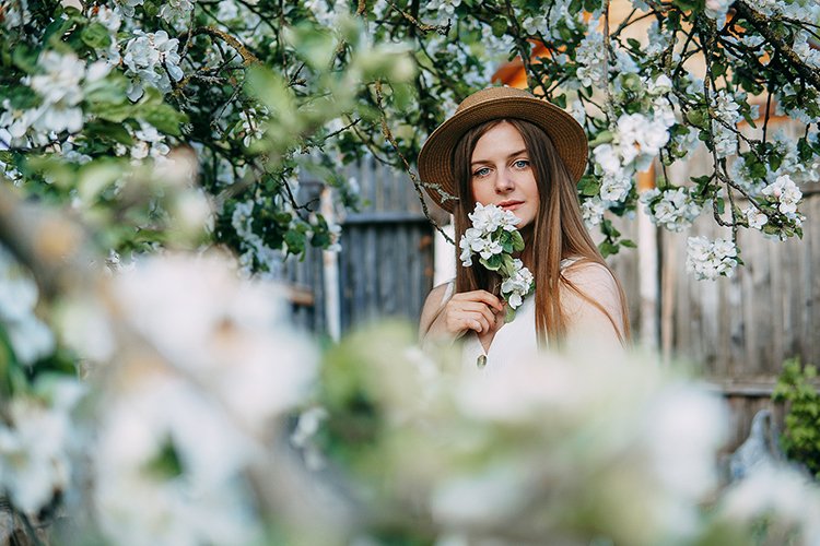 Beautiful young girl in hat in blooming Apple orchard.