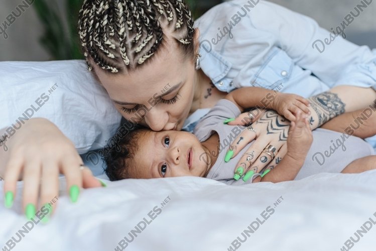 Modern caucasian woman kissing her baby while lying in bed