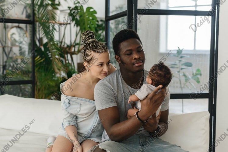 Young multiethnic family looks at the baby example image 1