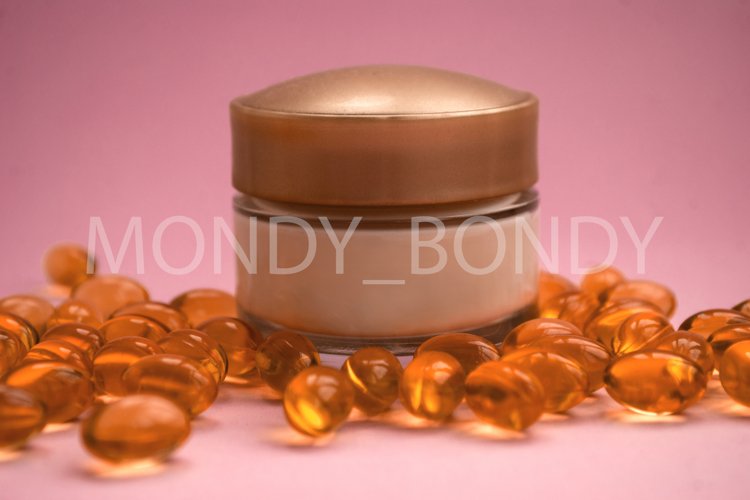 Bottle of cream with oil capsules on a pink background.