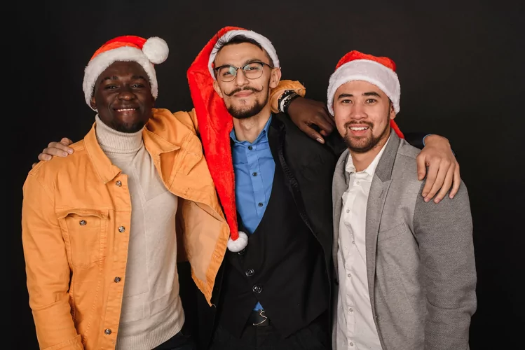 Black and Asian men in santa hats stand against a background