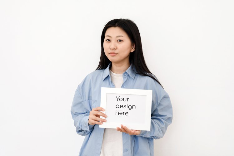 Asian woman holding white blank frame with mock up example image 1