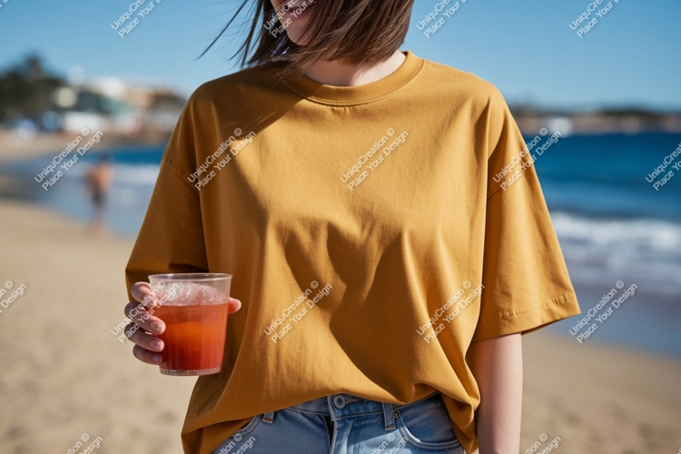 Woman wearing mustard t shirt holding drink on beach