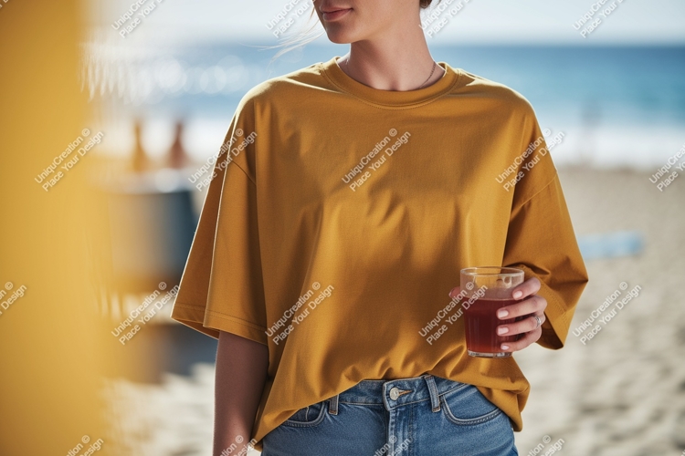 Woman wearing mustard t shirt holding drink on beach