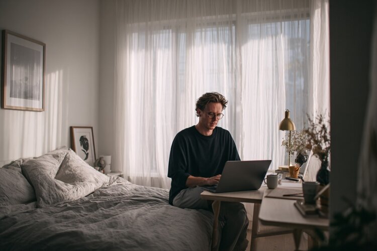 Young Man Working Remotely on Laptop in Cozy Bedroom example image 1