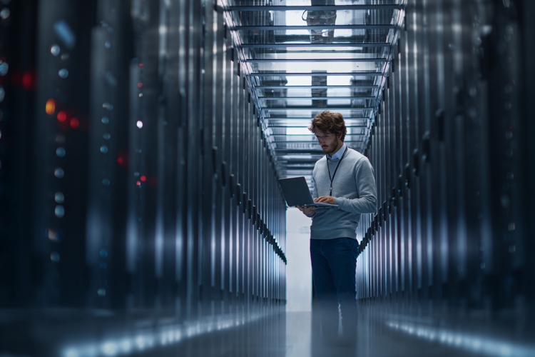 Man in Server Room Working on Laptop with Data Center Racks