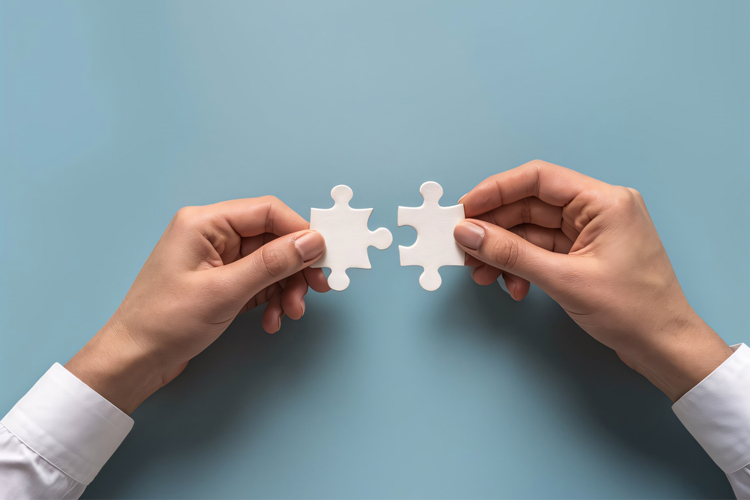 Two hands connecting puzzle pieces, symbolizing teamwork and